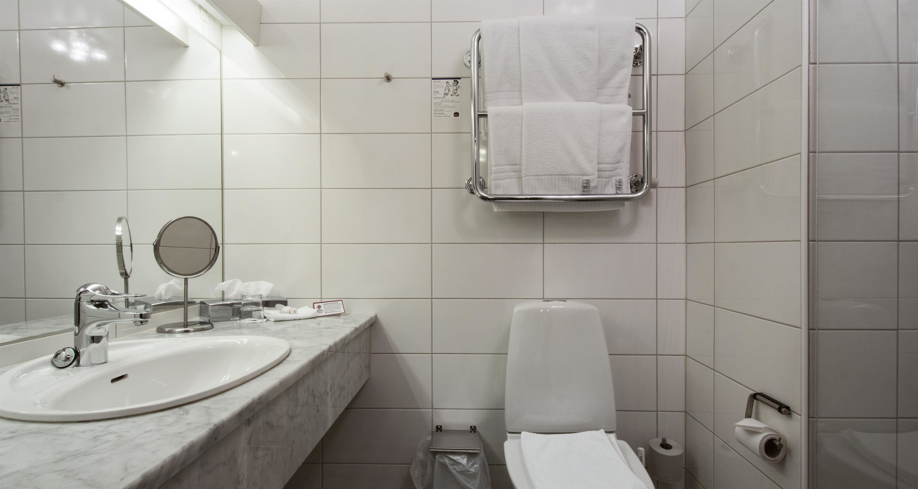 A bathroom with a sink, mirror, towel rack, toilet, and toilet paper.