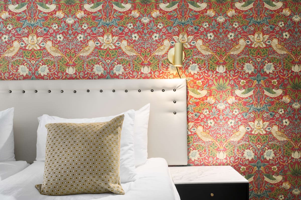 A hotel room with a patterned wallpaper, a white headboard, and a decorative wall sconce.