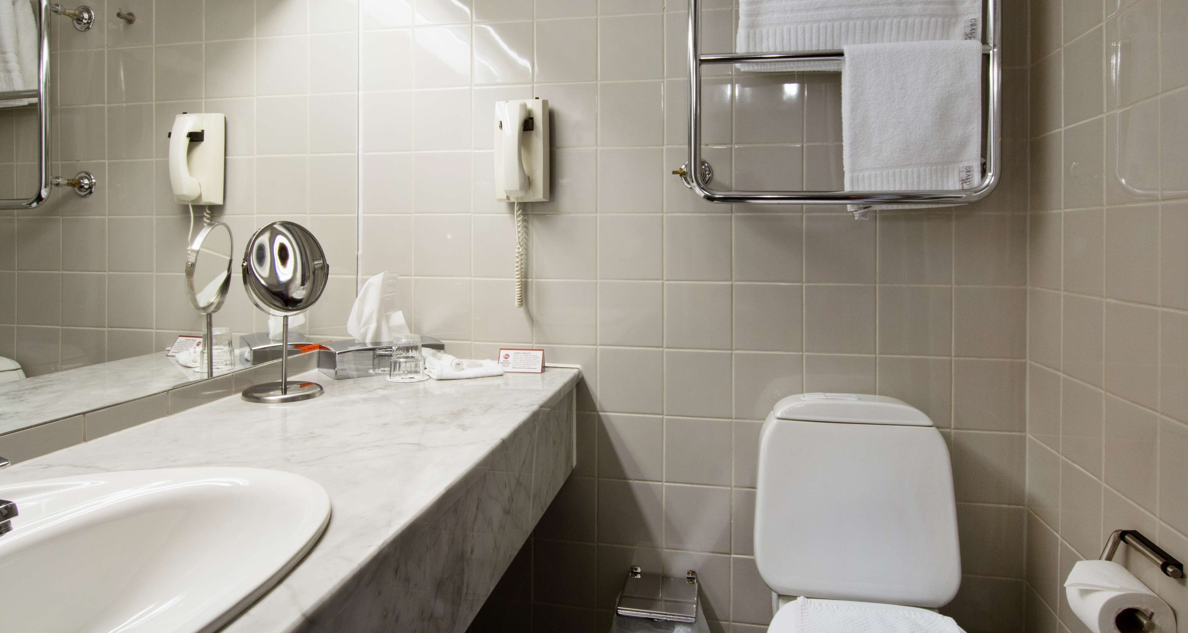 A bathroom with a marble countertop, a sink, a toilet, a mirror, a towel rack, and a telephone.