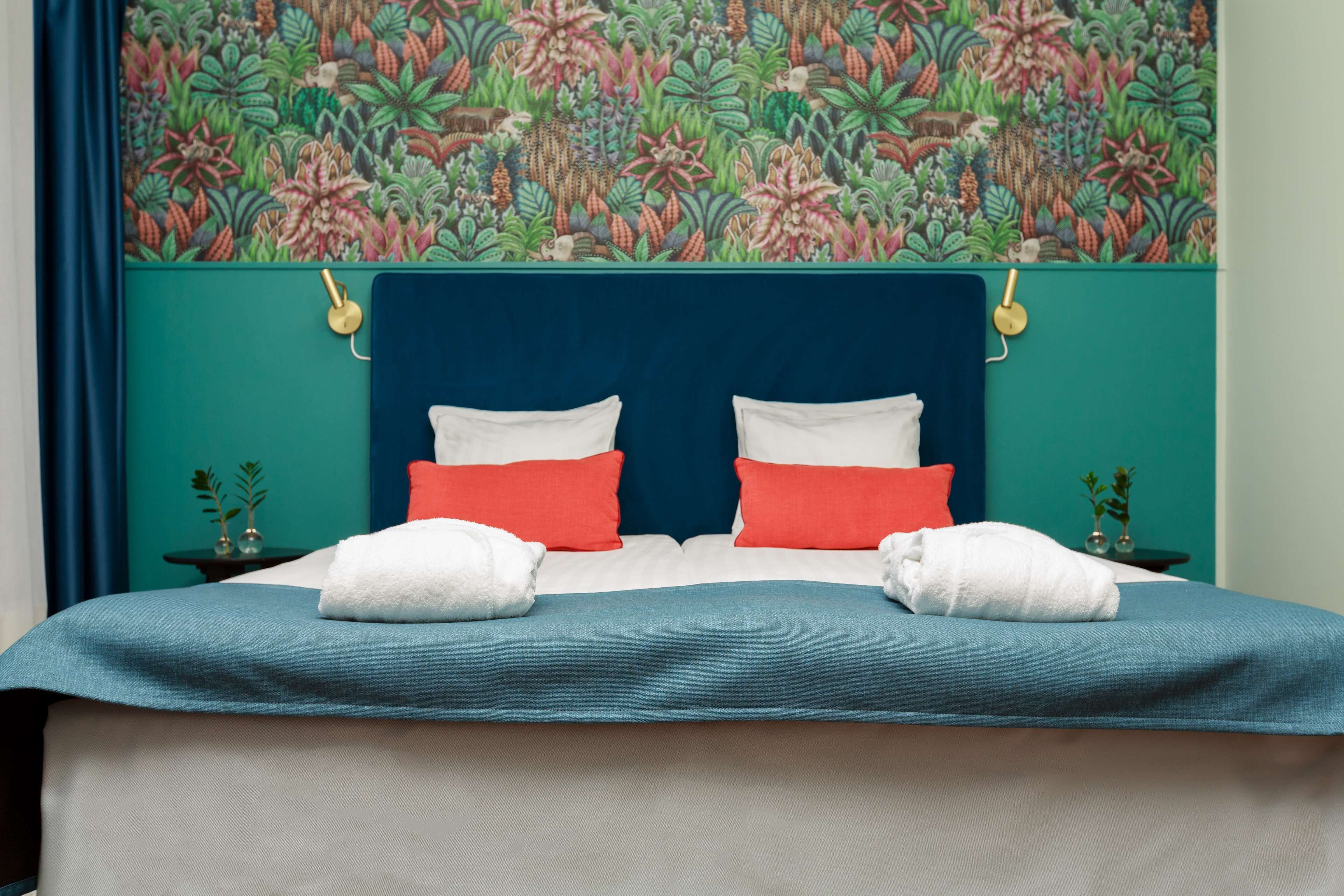 A bed with a teal headboard, white and red pillows, and two white towels.