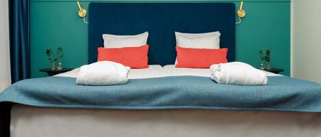 A bed with a teal headboard, white and red pillows, and two white towels.