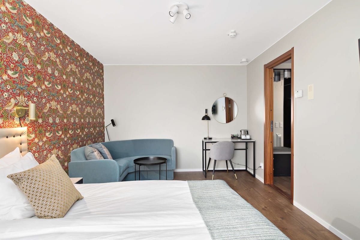 A bedroom with a bed, a blue sofa, a desk, and a mirror.