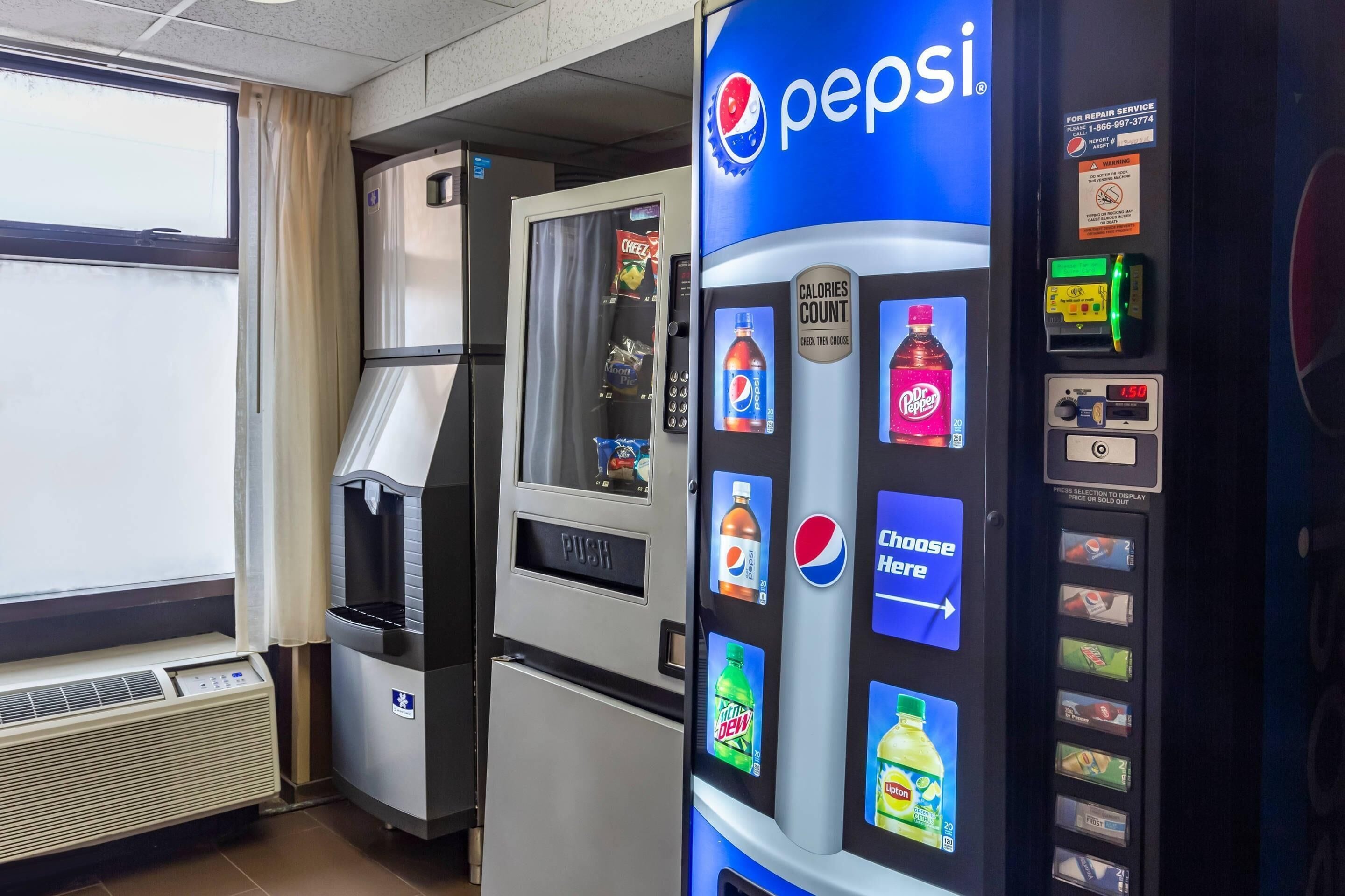 A vending machine with Pepsi branding and a digital display, a refrigerator, and a window with curtains.