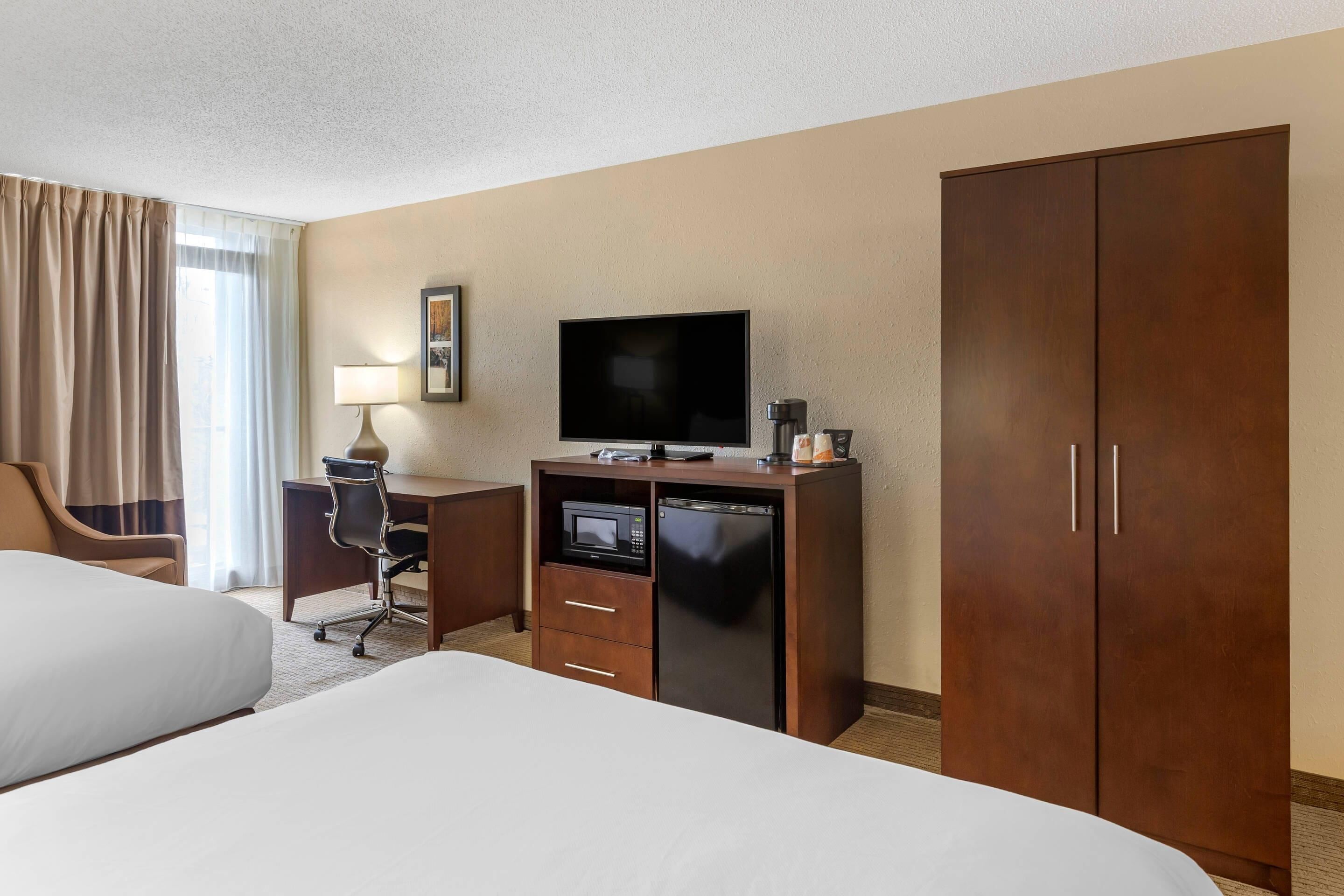 Habitación de hotel con cama, escritorio con televisor, microondas, refrigerador y armario.