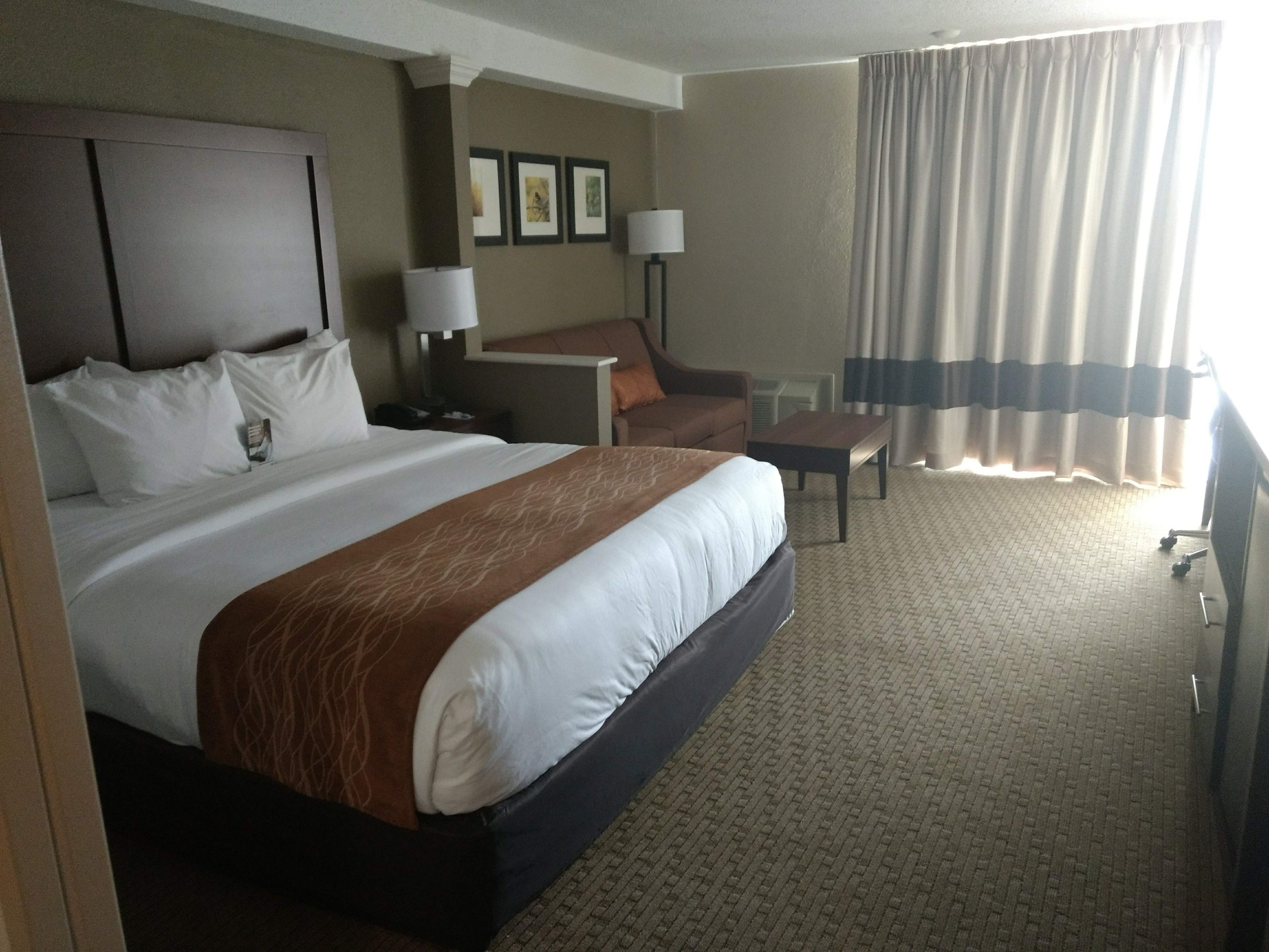 Ein Hotelzimmer mit einem großen Bett, einem Schreibtisch, einem Sessel und Blick ins Freie.