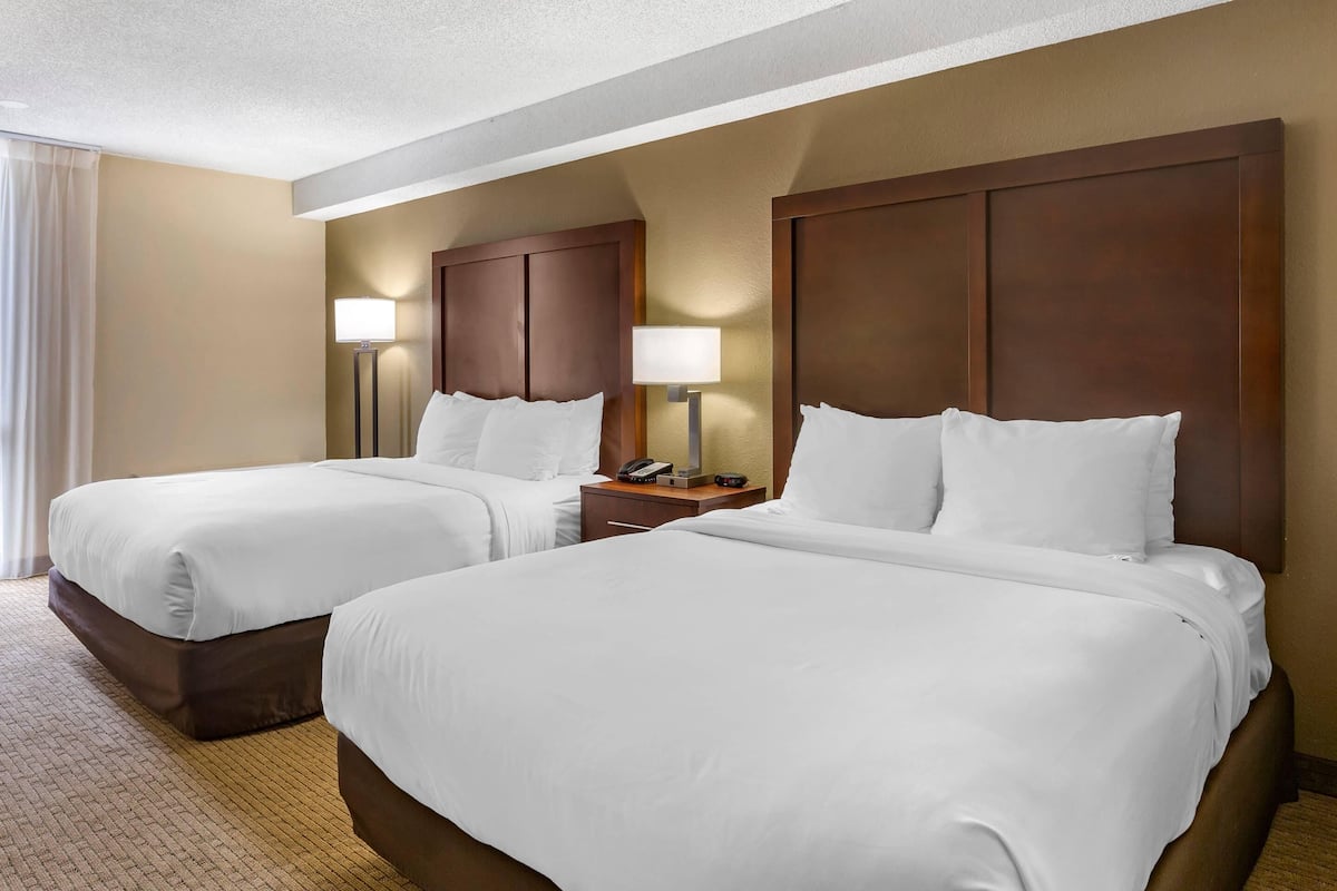 A hotel room with two beds, a nightstand with a lamp, and a telephone.