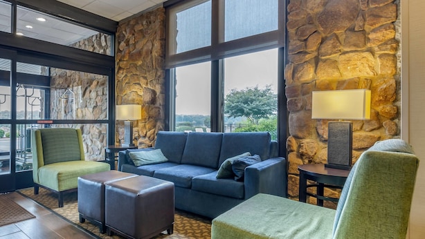 A modern lobby with a stone wall, a blue sofa, green armchairs, and a patterned rug.