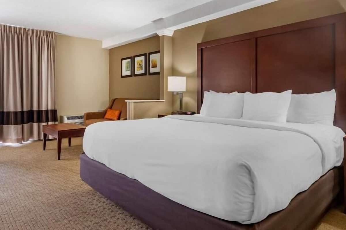 A hotel room with a large bed, a desk, a chair, a lamp, and a nightstand.