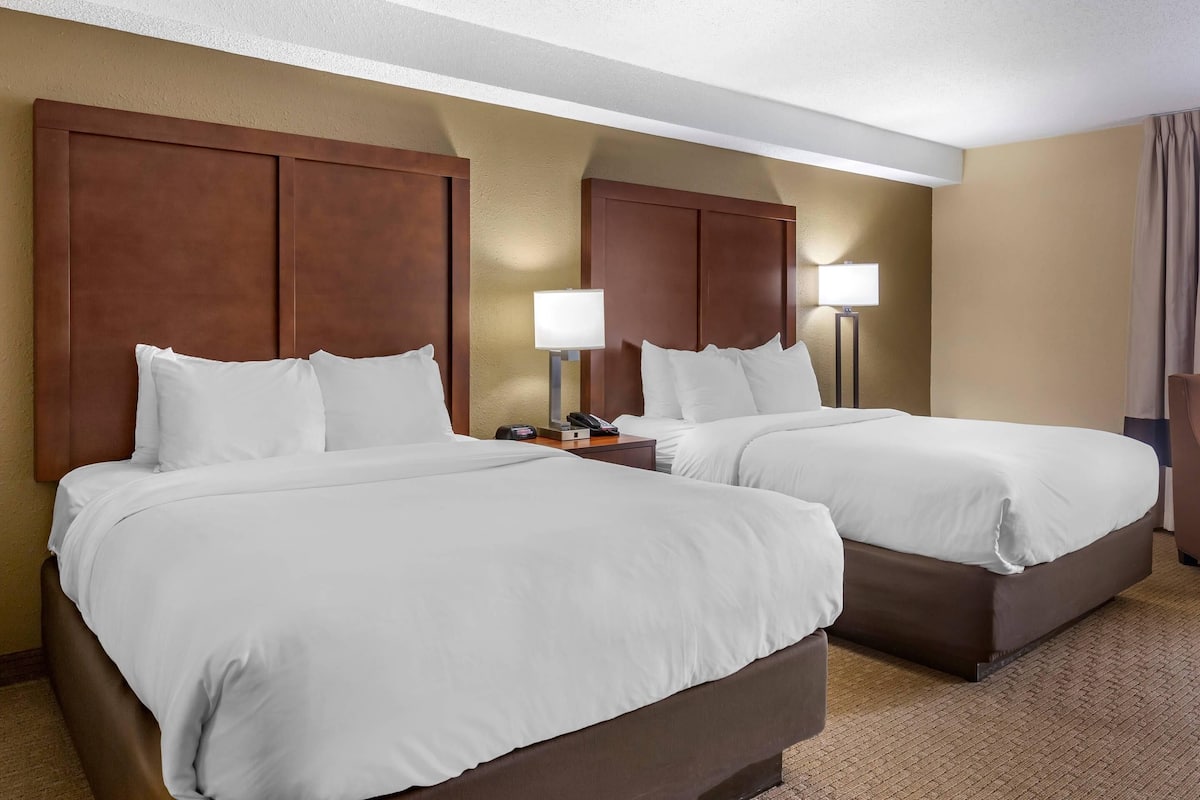 A hotel room with two beds, a nightstand with a lamp, and a telephone.