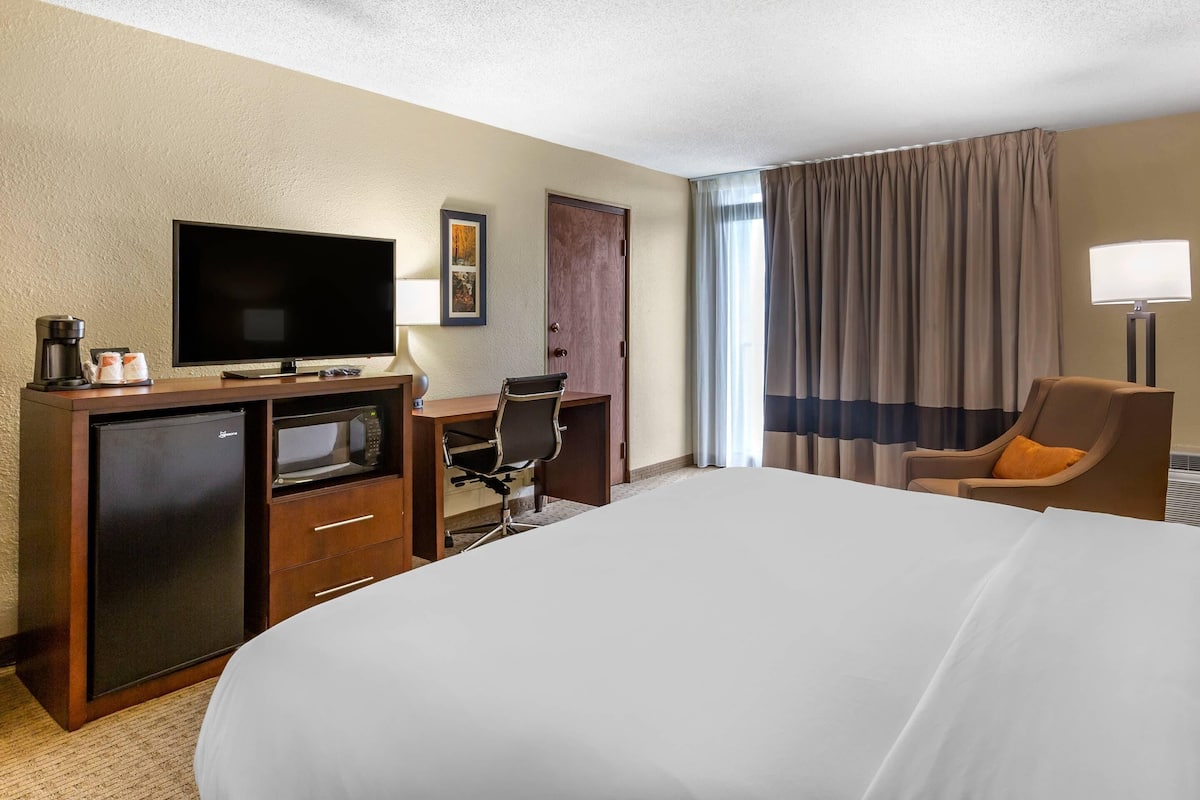 A hotel room with a bed, a desk with a computer, a television, a mini-fridge, and a lamp.
