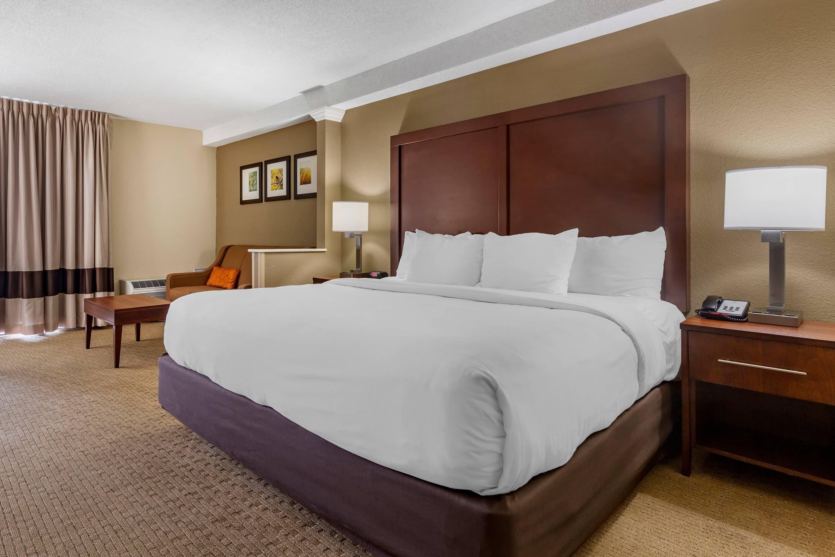 Una habitación de hotel con una cama grande, una mesita de noche con lámpara, una silla y un escritorio.
