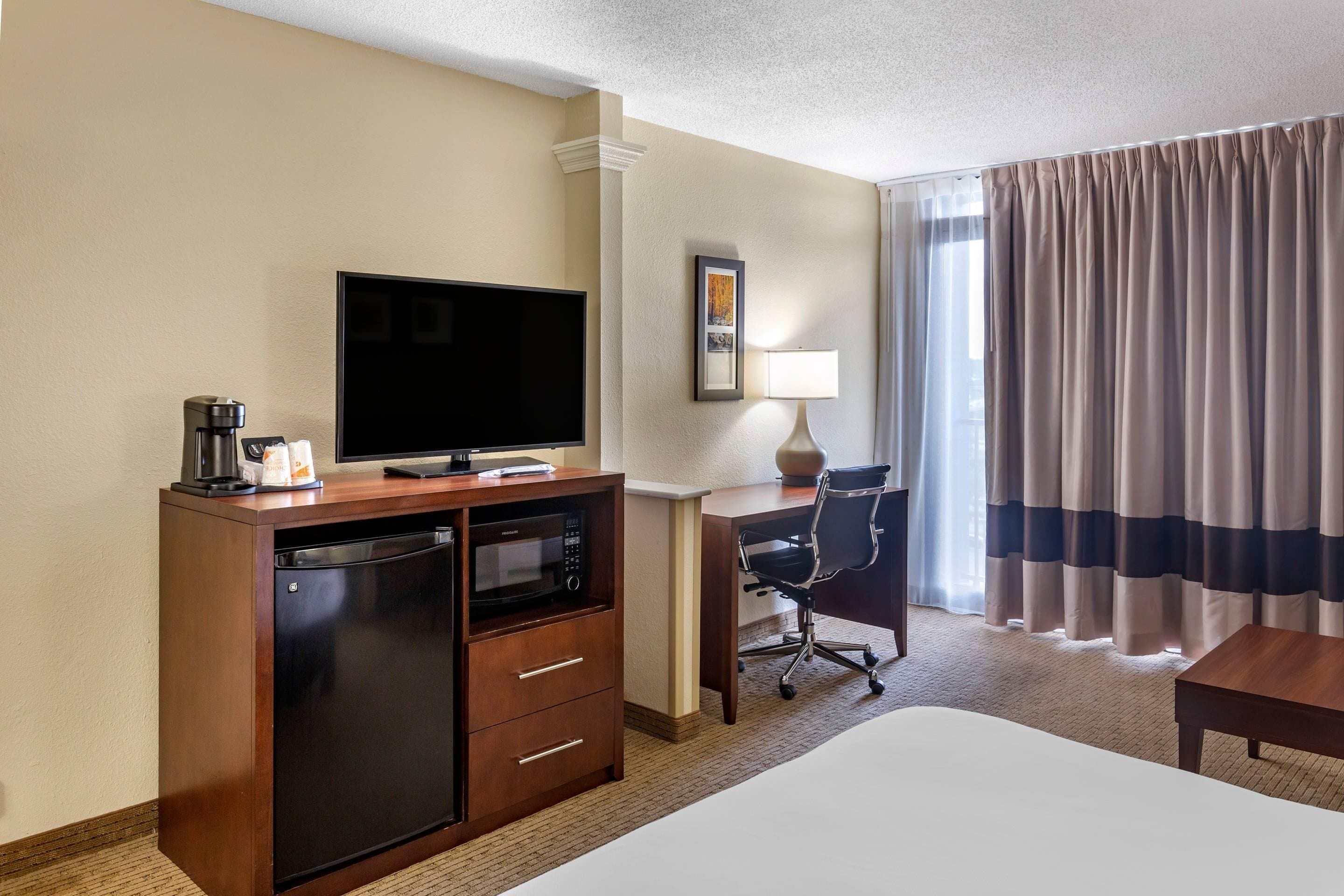 Une chambre d’hôtel équipée d’un lit, d’un bureau avec une chaise, d’une télévision, d’une machine à café et d’un four à micro-ondes.