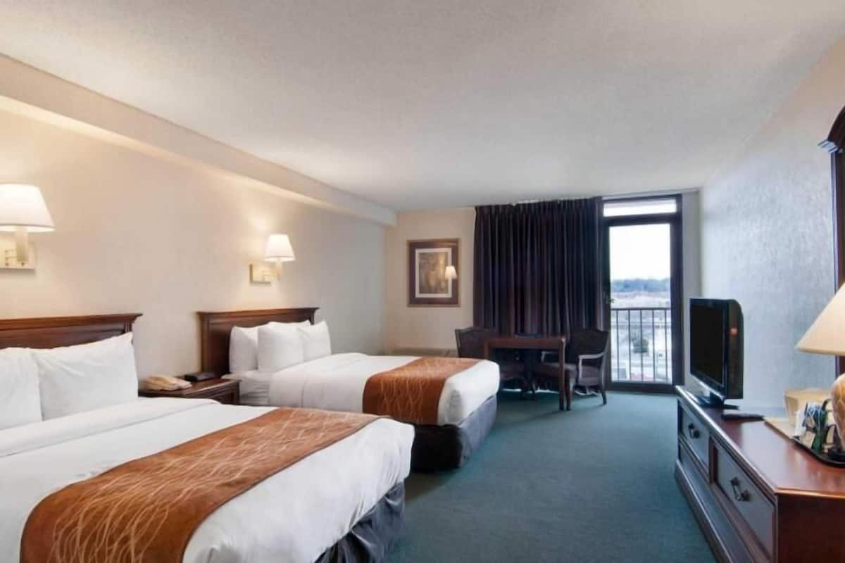 A hotel room with two beds, a desk, a television, and a view through the window.