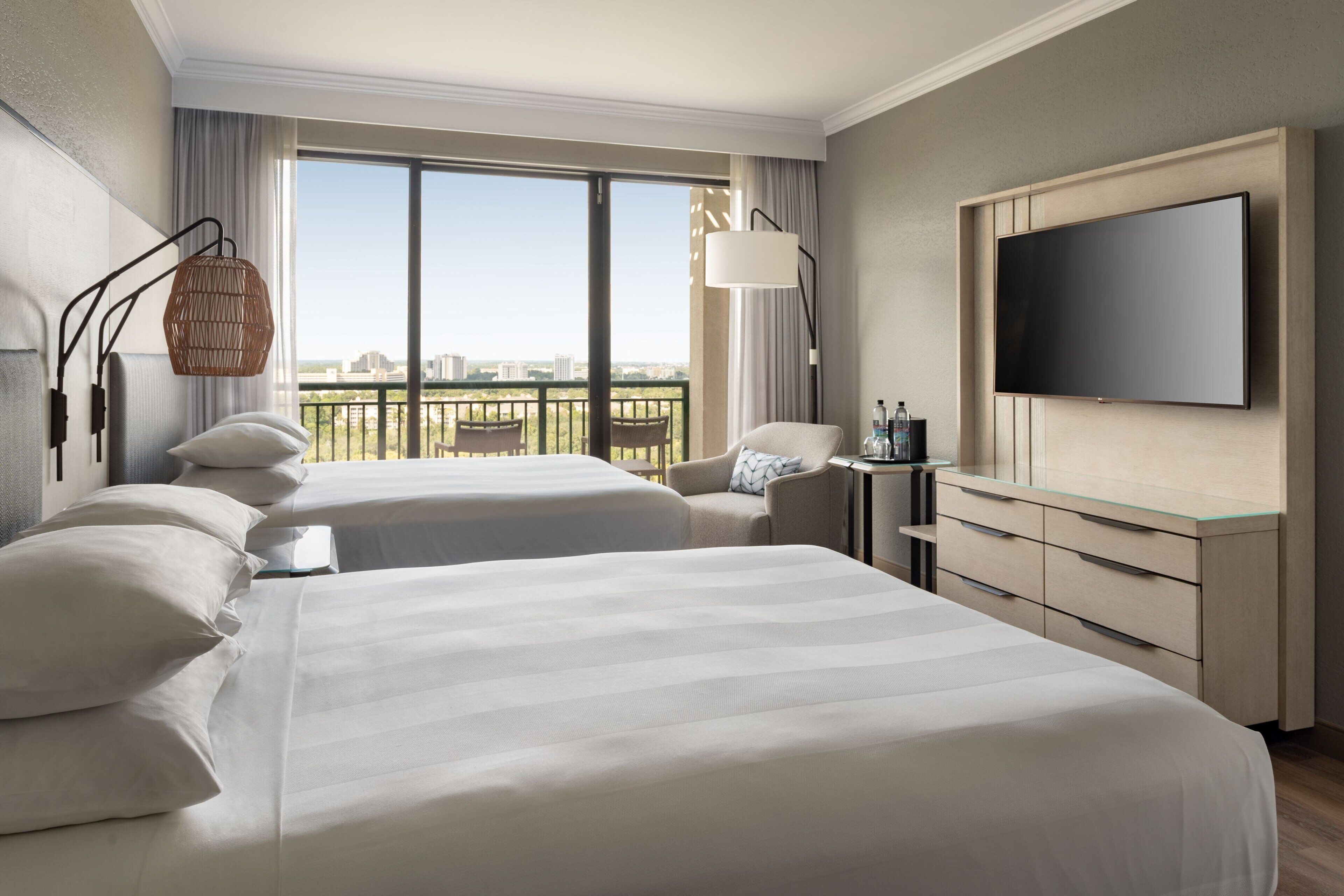 Ein Hotelzimmer mit zwei Betten, einem Fernseher, einem Schreibtisch und einem Balkon mit Stadtblick.