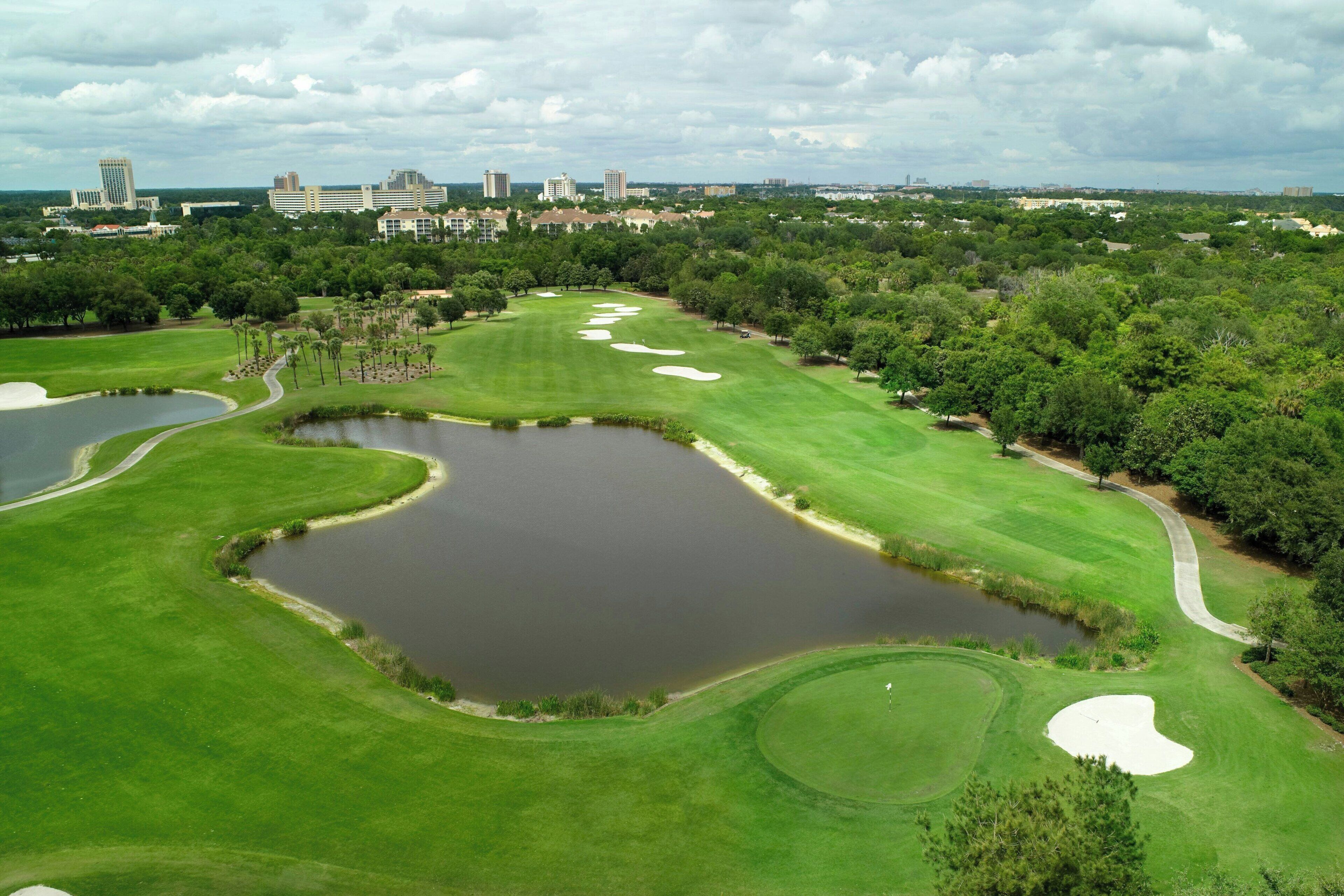 A golf course with sand bunkers, water hazards, and a city skyline in the background.