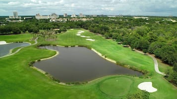 A golf course with sand bunkers, water hazards, and a city skyline in the background.