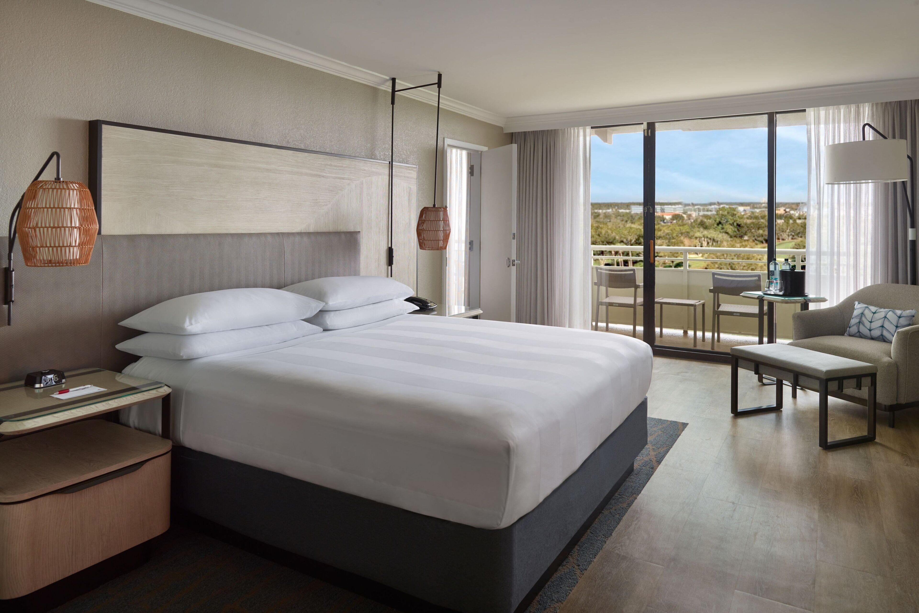 A hotel room with a large bed, a bedside table, a chair, and a view of the outdoors.