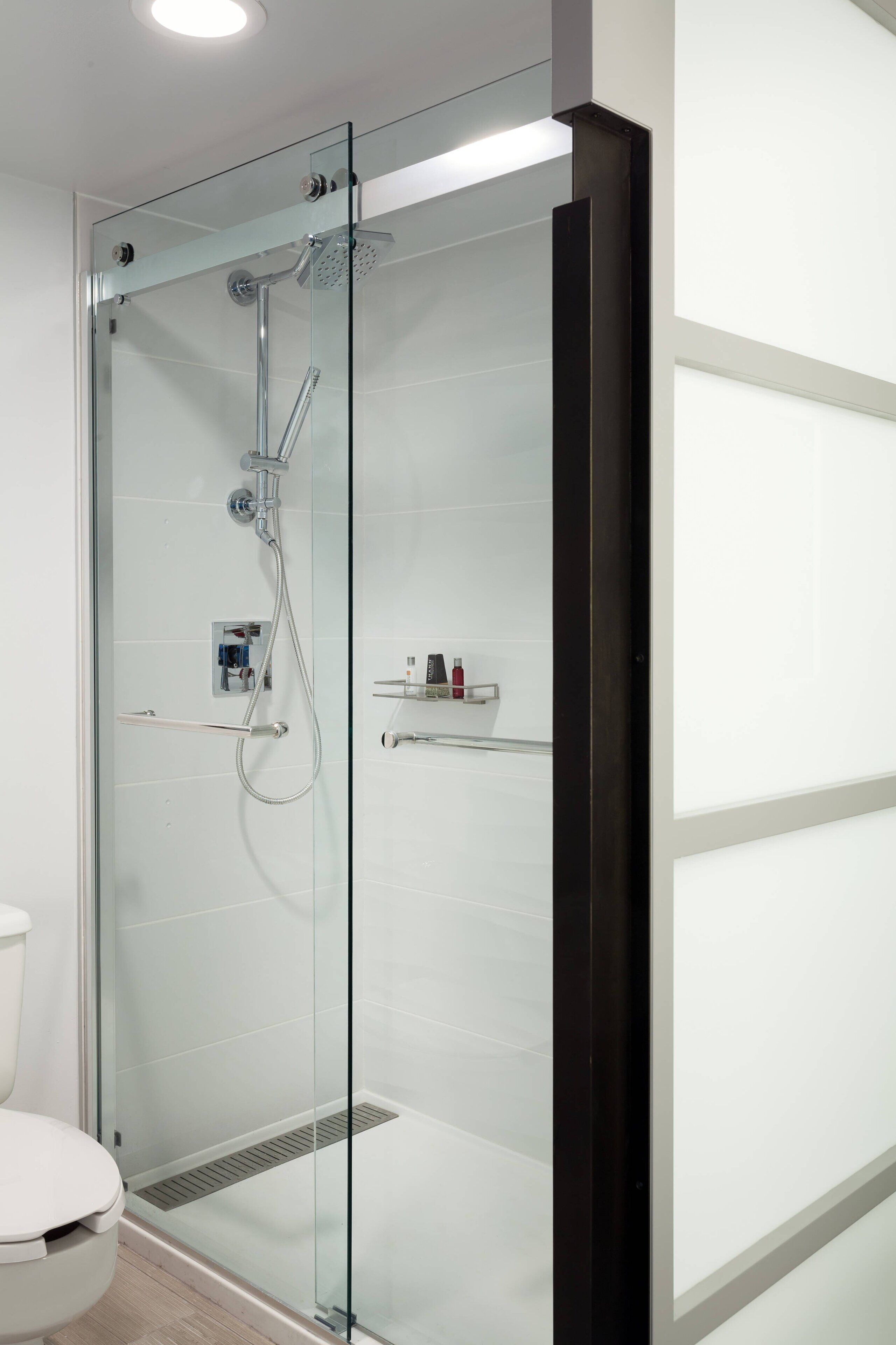 Un baño moderno con ducha de vidrio, inodoro y repisa con artículos de aseo.