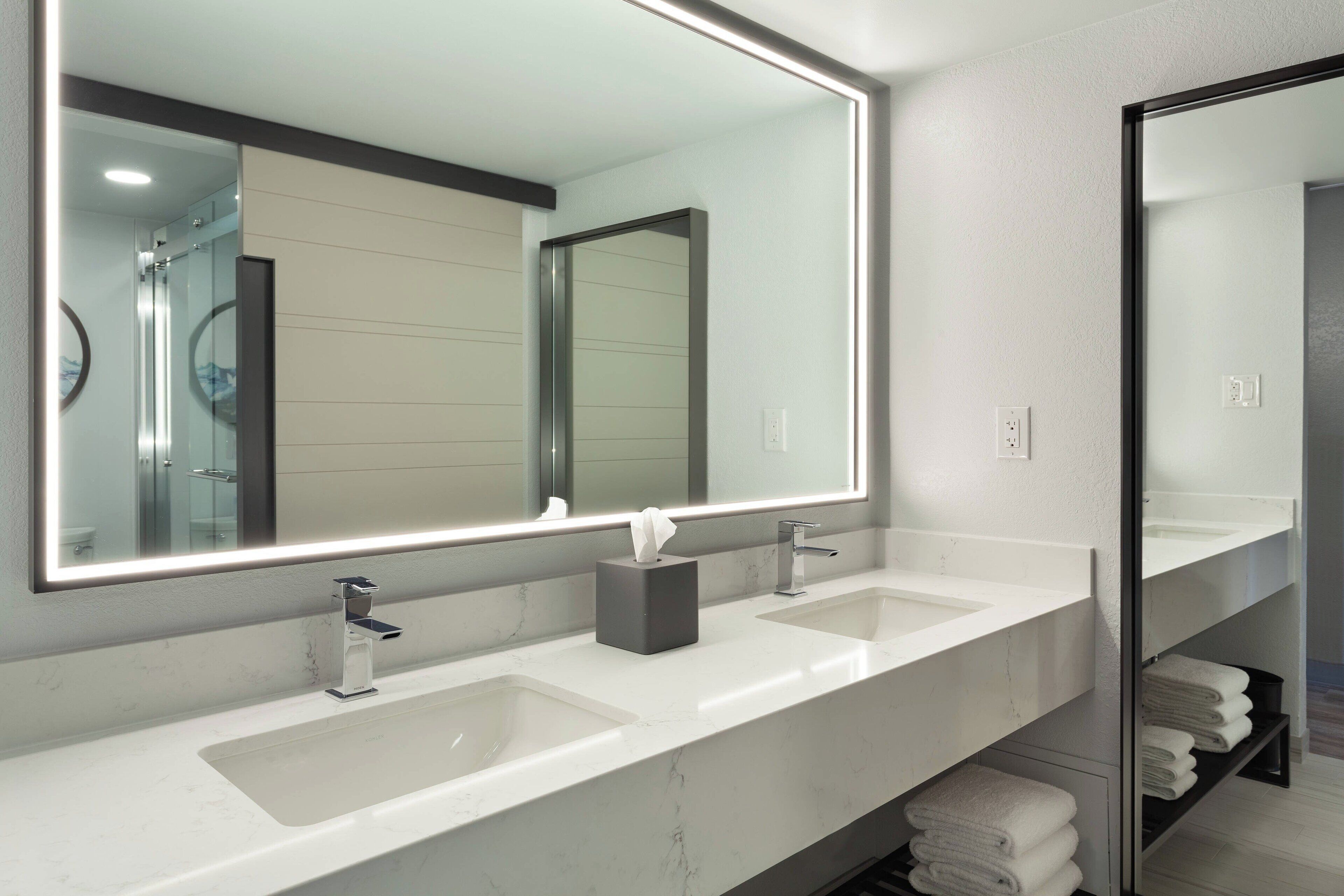 A modern bathroom with two sinks, a large mirror, and a towel rack.