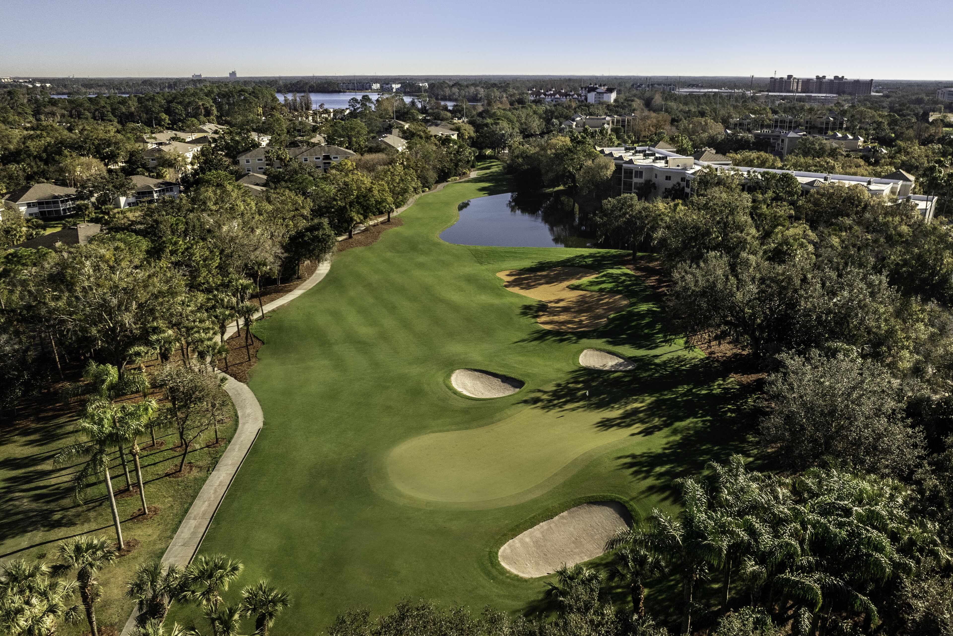 A golf course with sand bunkers, a water hazard, and surrounding residential buildings.
