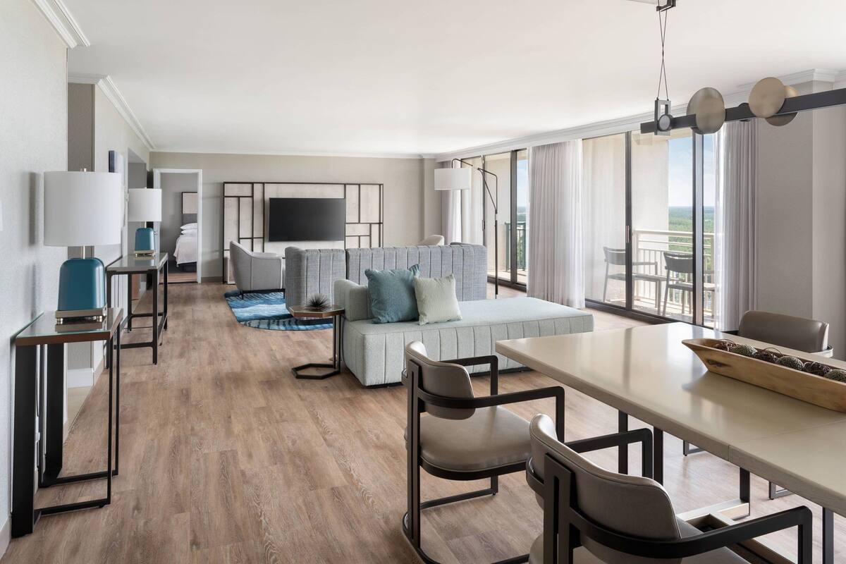 A modern hotel room with a sofa, dining table, and TV.