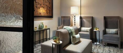A modern hotel room with a sofa, armchairs, a lamp, a painting, and a small table with a plant.