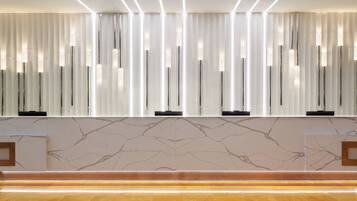 Una zona de recepción moderna con pared de mármol, lámparas verticales y un banco de madera pulida.