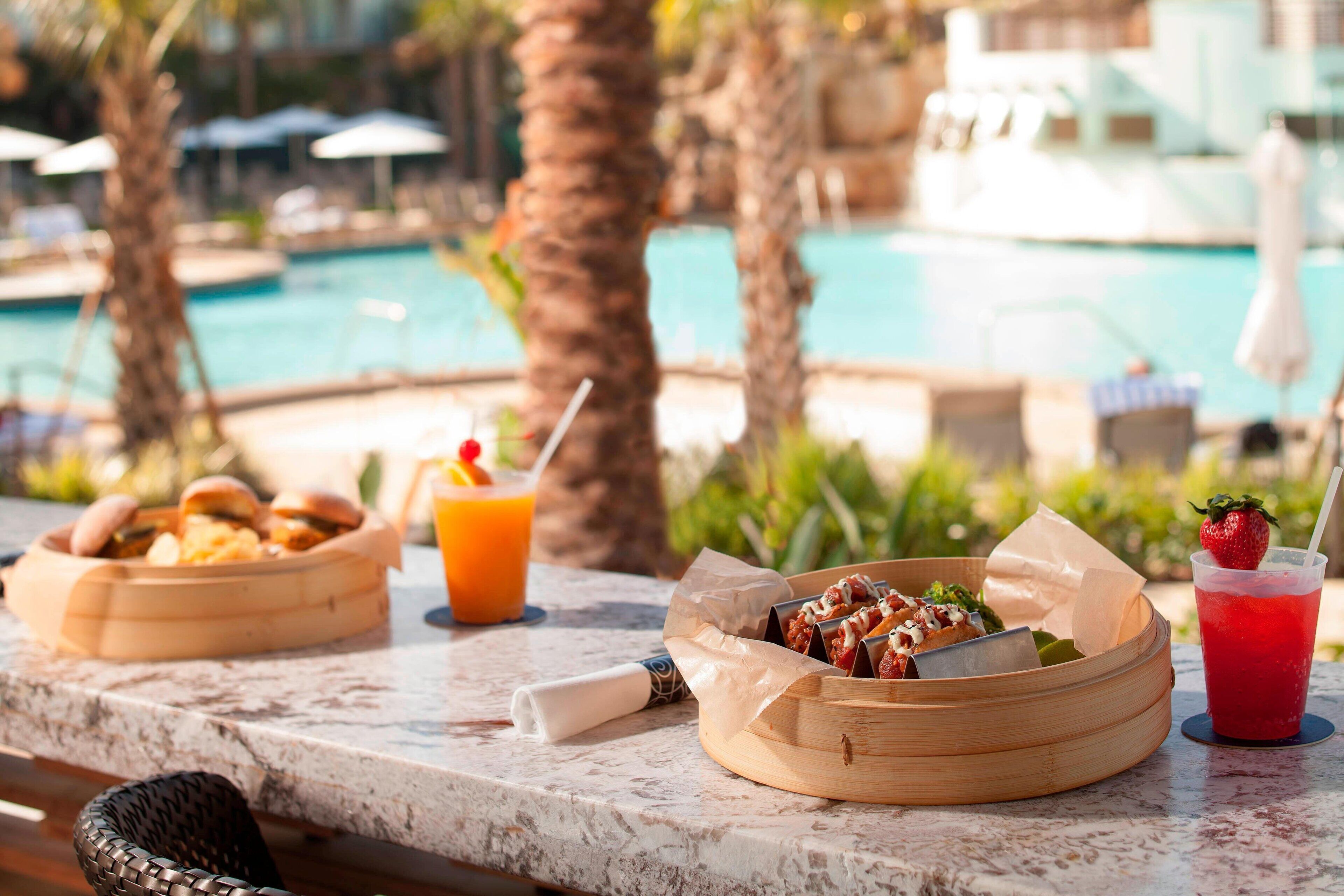A dining table with food and drinks, overlooking a pool.