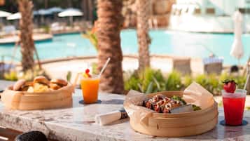 A dining table with food and drinks, overlooking a pool.