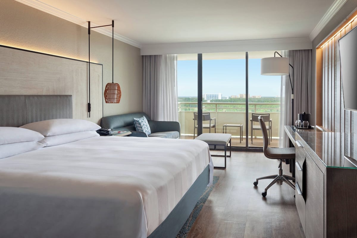 A hotel room with a large bed, a desk, a chair, and a view of the city.