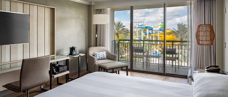 Una habitación de hotel con una cama grande, un escritorio, una silla, un televisor y un balcón con vistas a un parque acuático.
