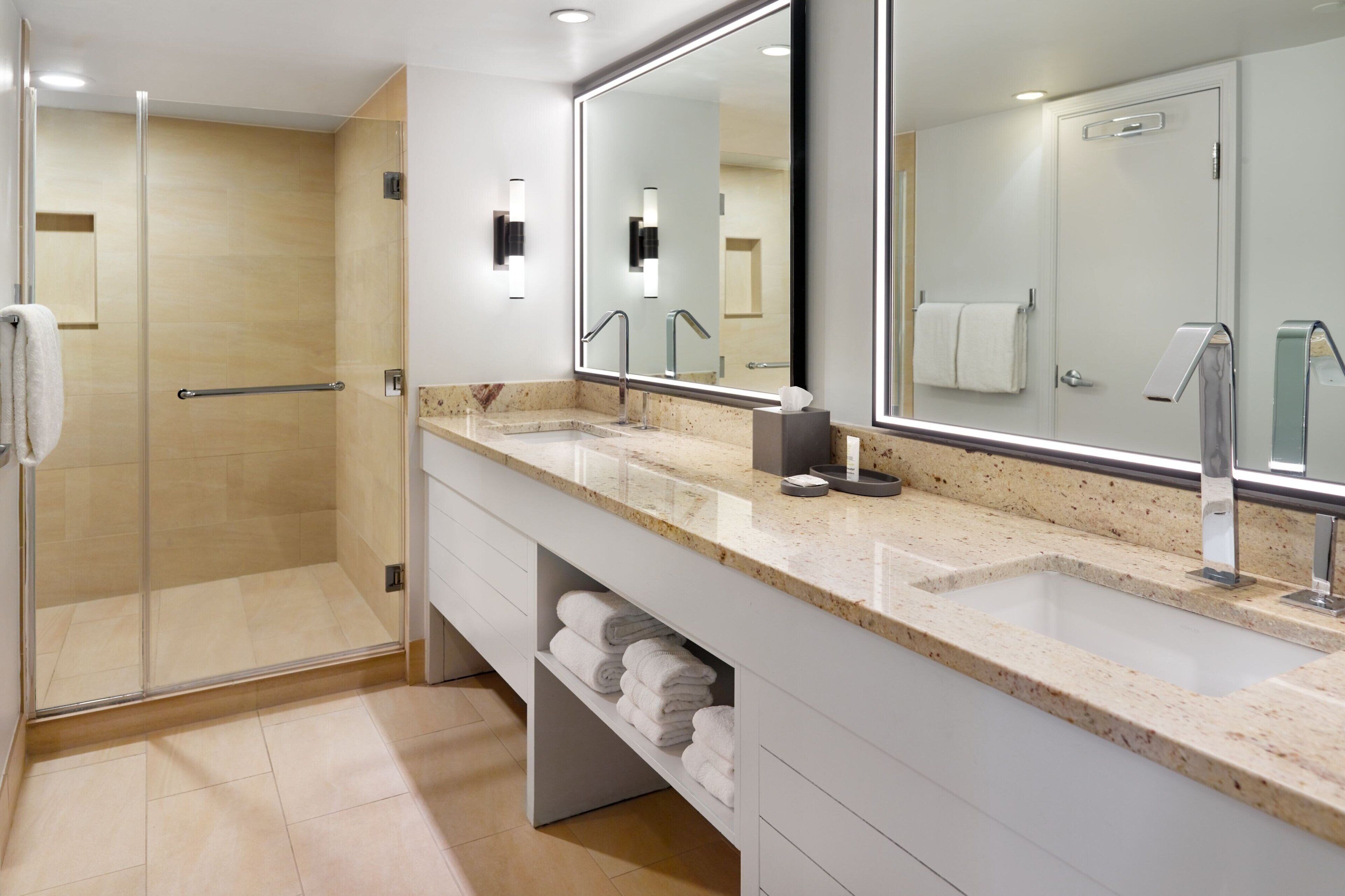 A modern bathroom with a glass shower enclosure, a large mirror, and a vanity with a sink and towel storage.