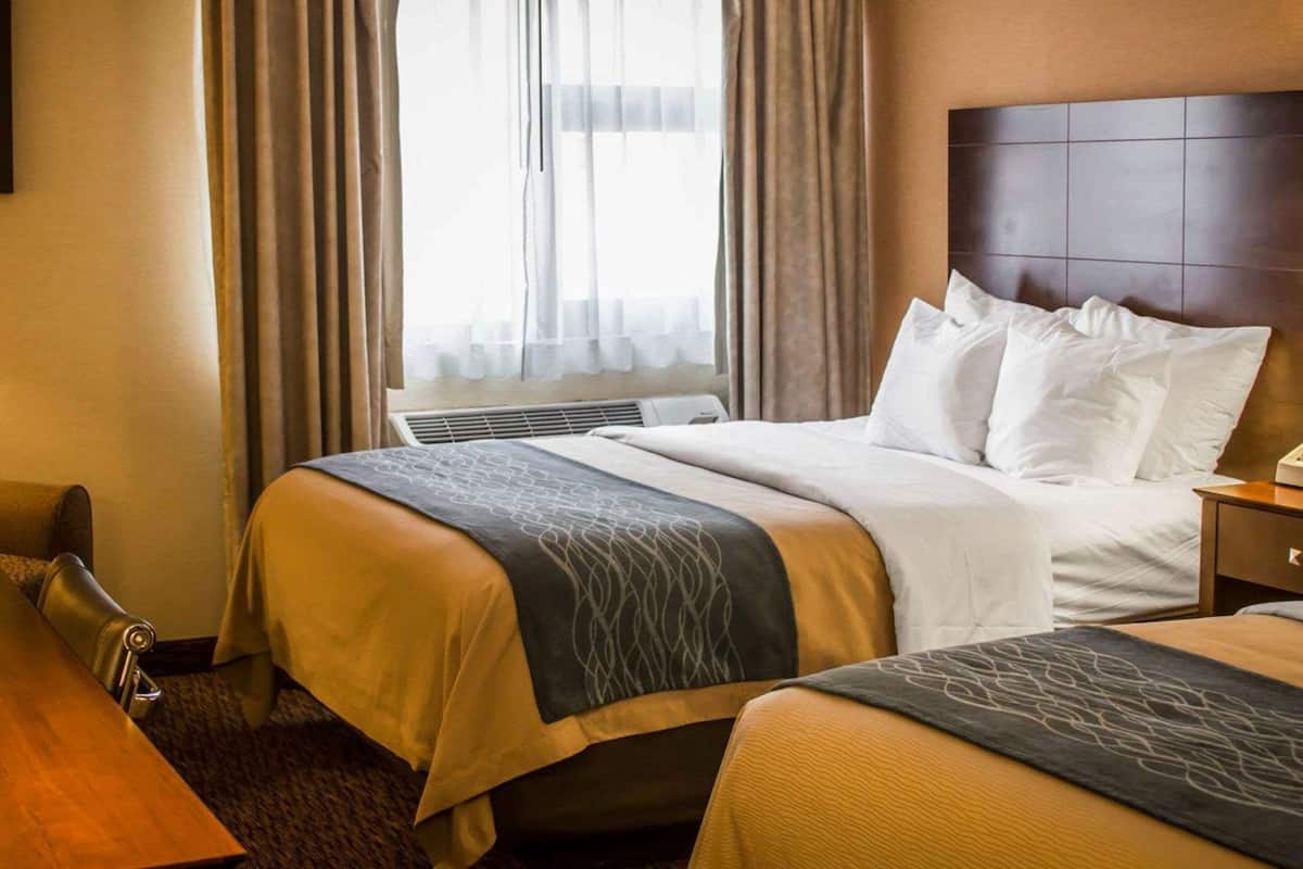 A hotel room with a large bed, a smaller bed, a desk, and a window with curtains.