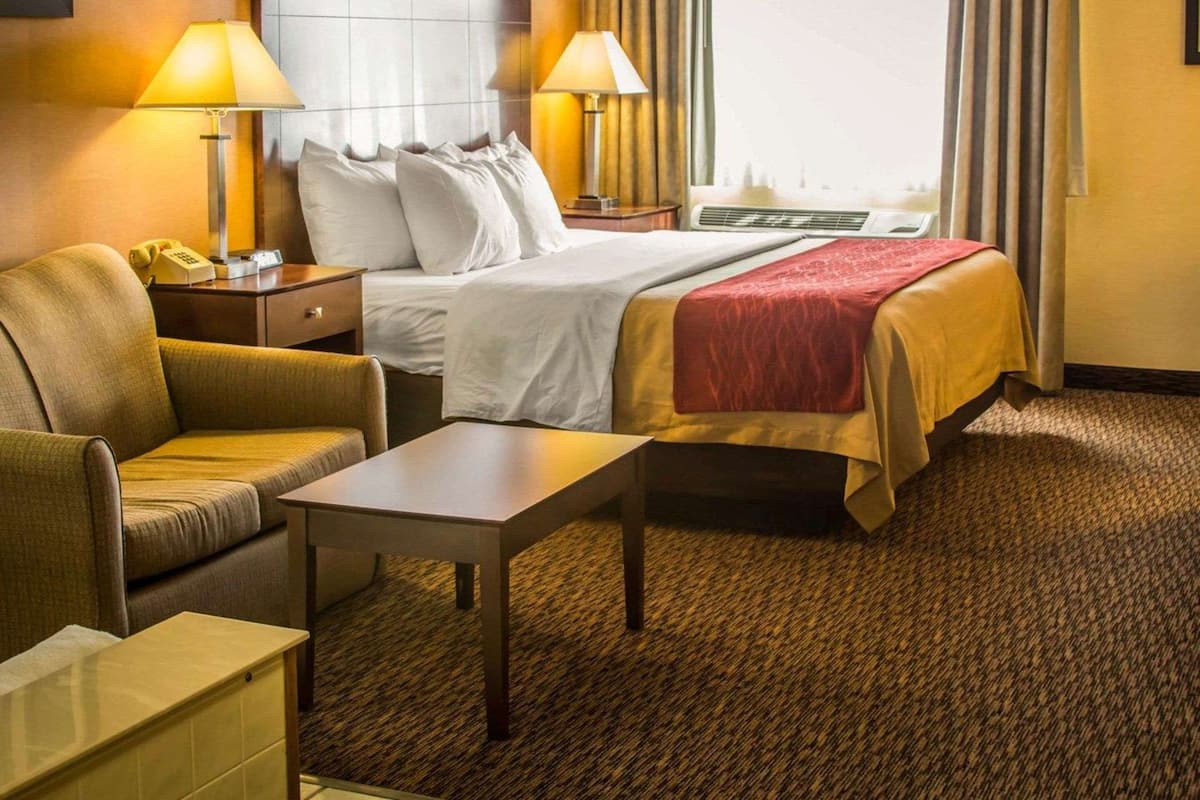 A hotel room with a bed, two bedside lamps, a nightstand, a desk, a chair, and a window with curtains.