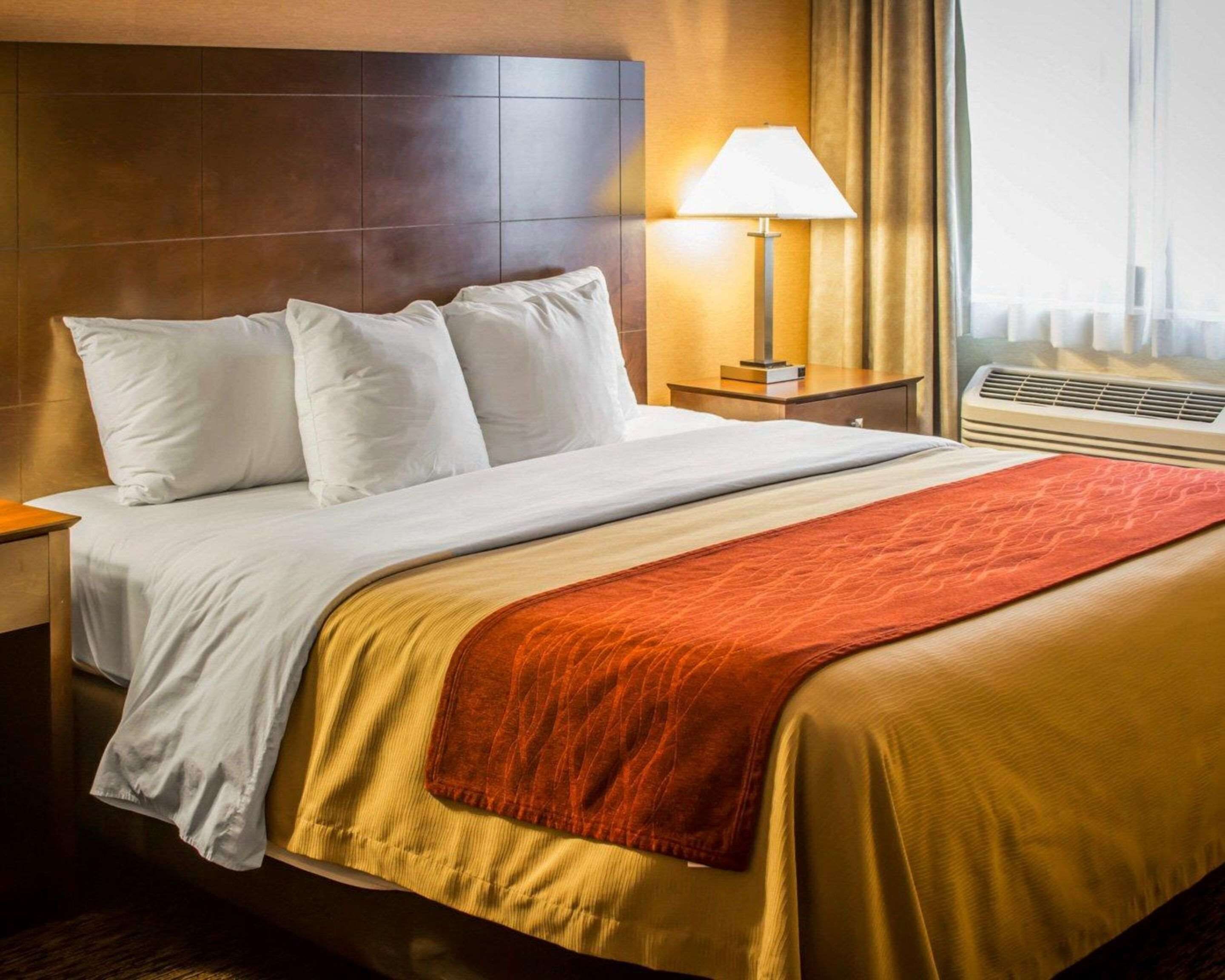 Quarto de hotel com cama, mesa de cabeceira, abajur e janela com cortinas.