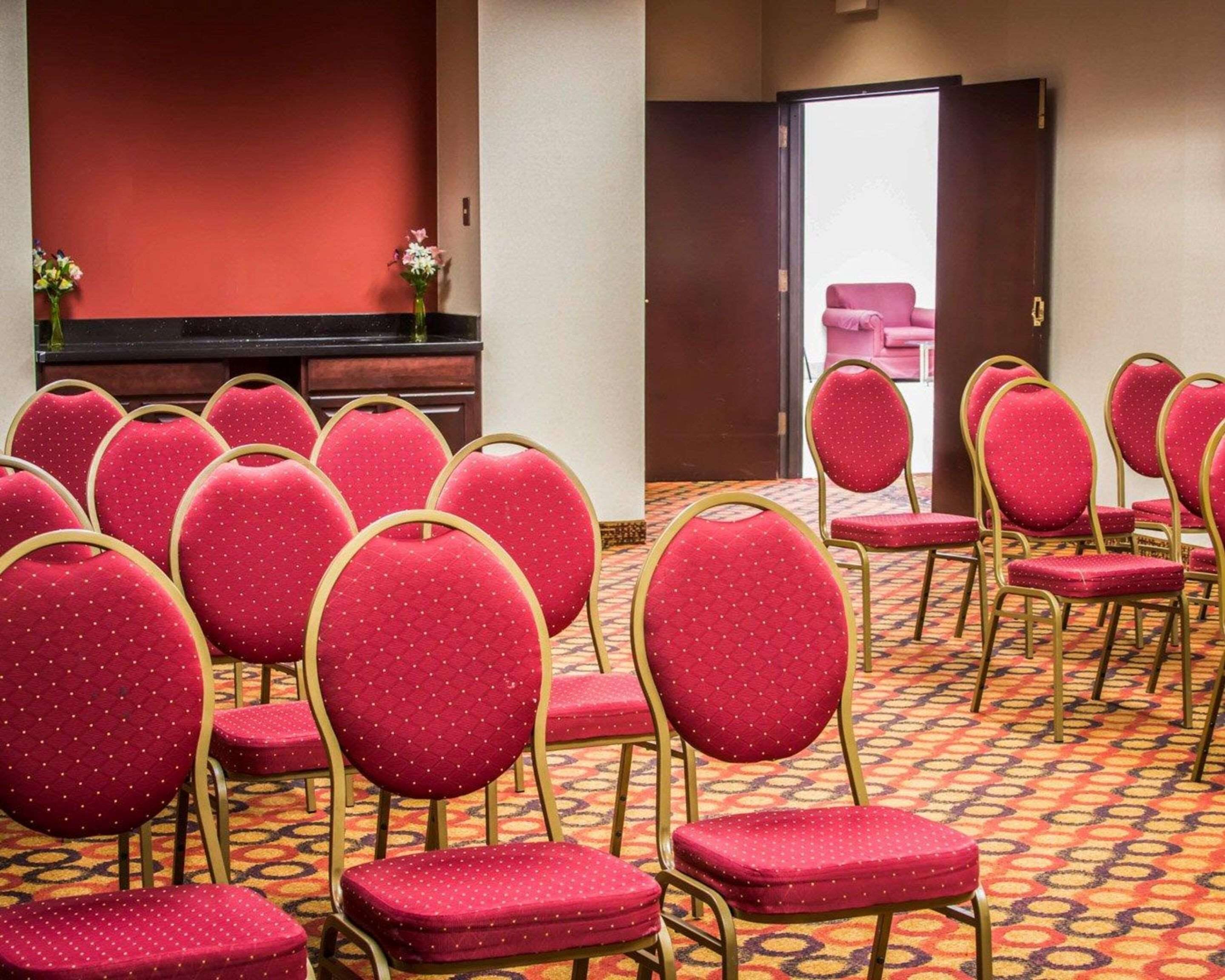 Une chambre d’hôtel avec des rangées de chaises rouges à cadre doré, un sol recouvert de moquette et un mur rouge.