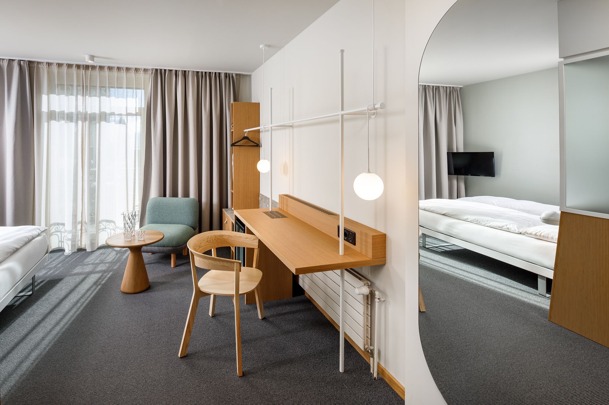 Une chambre d’hôtel comprenant un lit, un bureau avec une chaise, une petite table et un téléviseur fixé au mur.
