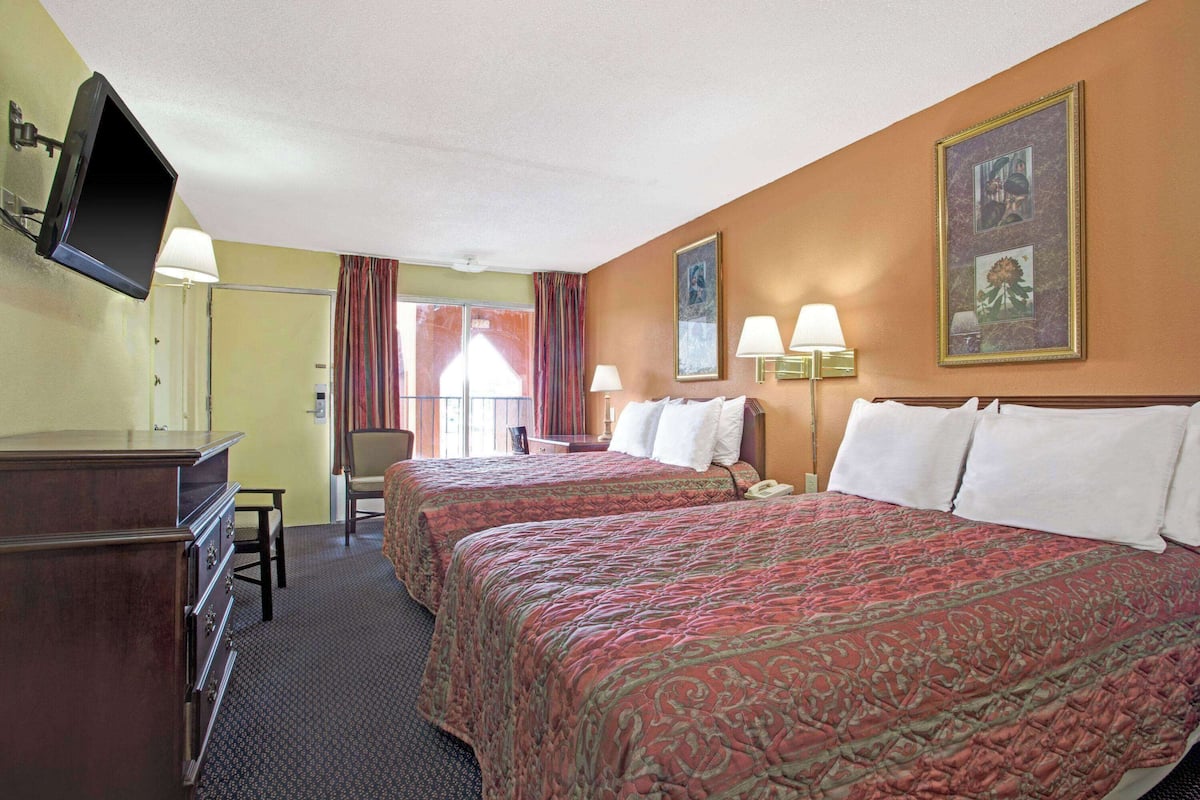 A hotel room with two beds, a desk, a TV, and a window with curtains.