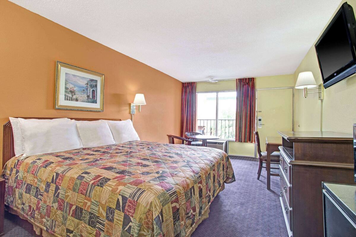 A hotel room with a large bed, a desk with a chair, a television, and a window with curtains.