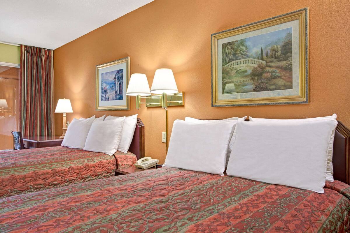 A hotel room with two beds, a telephone, wall-mounted lamps, and framed pictures.