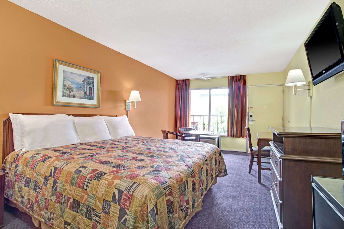 A hotel room with a bed, a desk, a chair, a television, and a window with curtains.