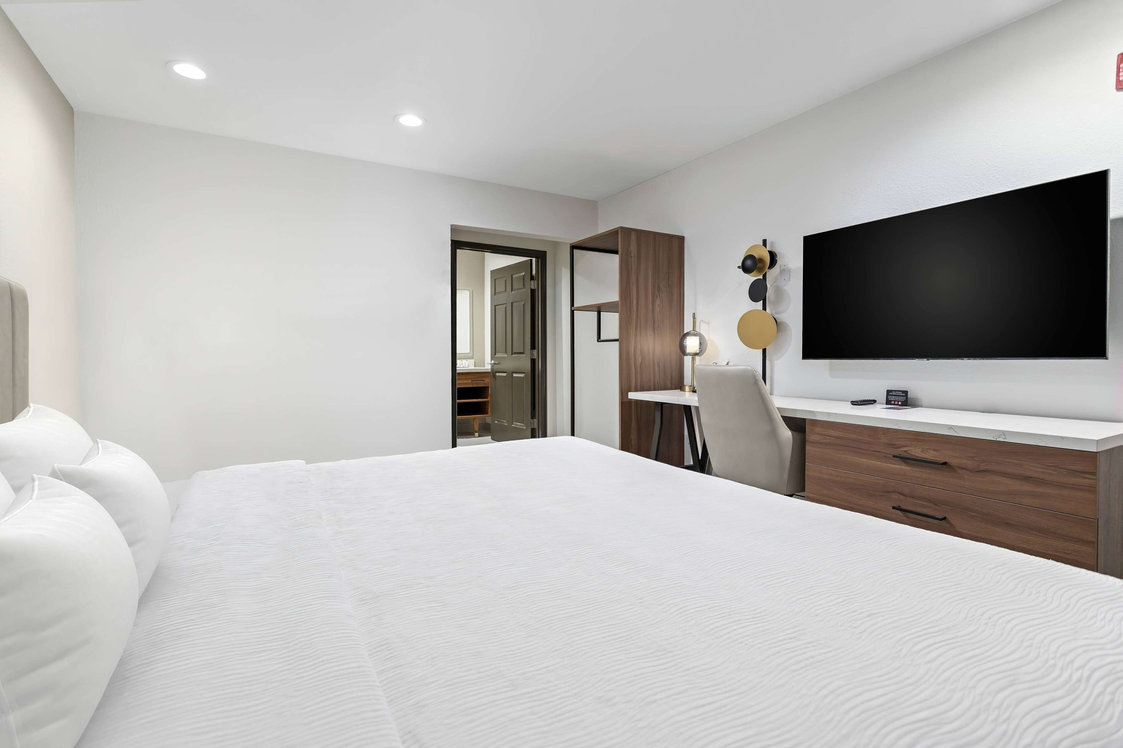 Una habitación de hotel moderna con una cama grande, un escritorio, un televisor de pantalla plana y un armario.
