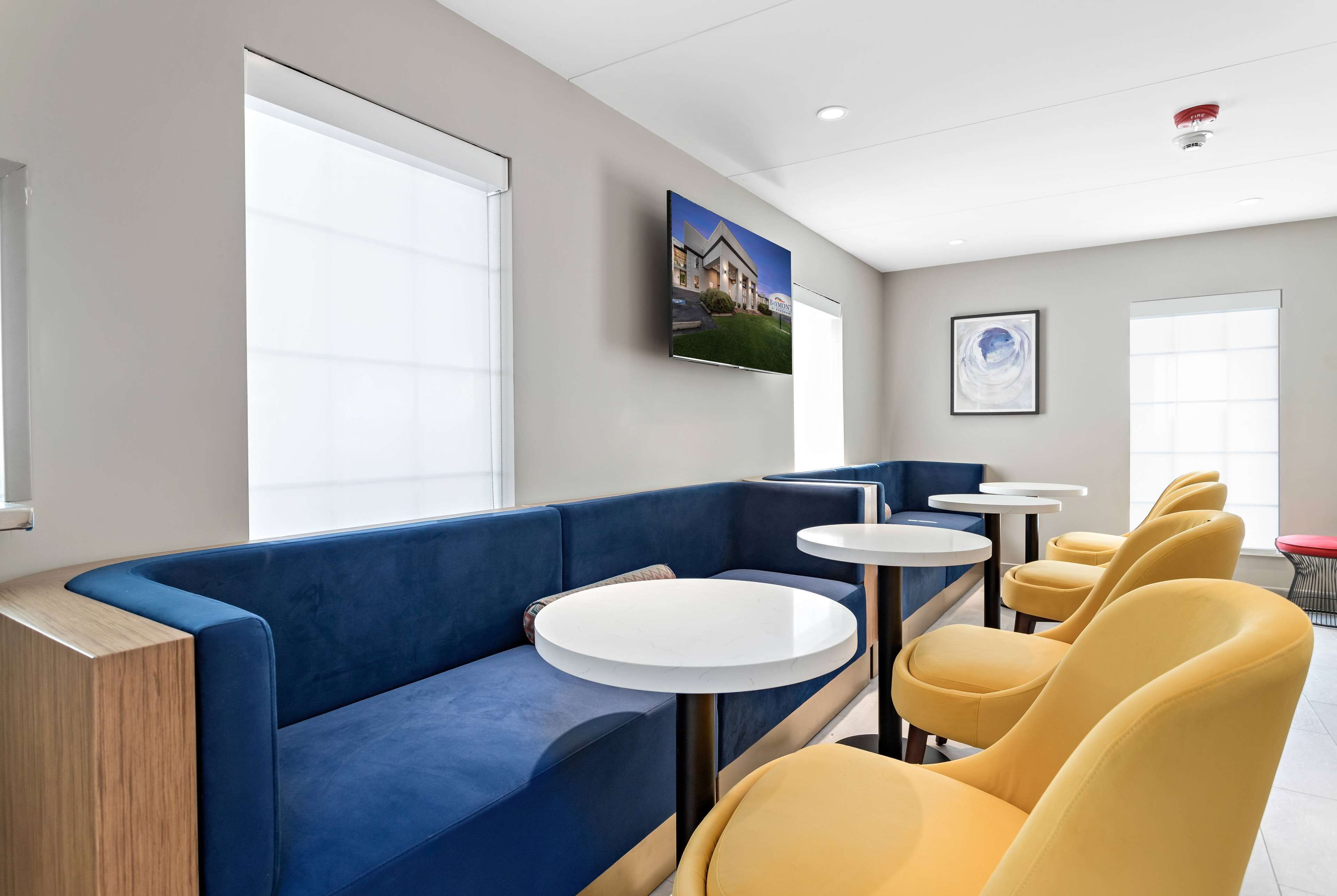A modern hotel lobby with a blue sofa, yellow chairs, and a television displaying a house.