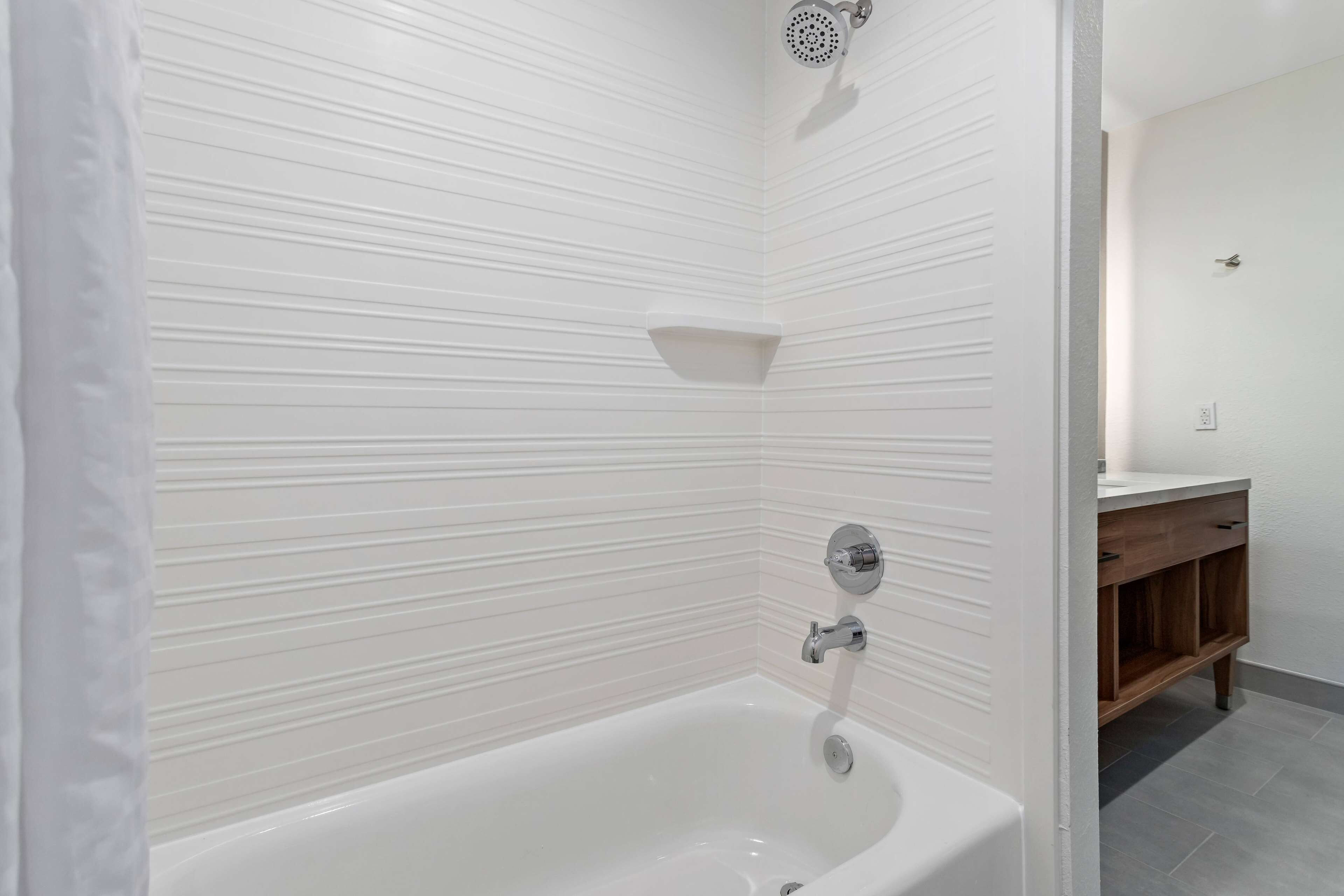 Un baño moderno con una bañera blanca, un cabezal de ducha y un mueble de tocador de madera.