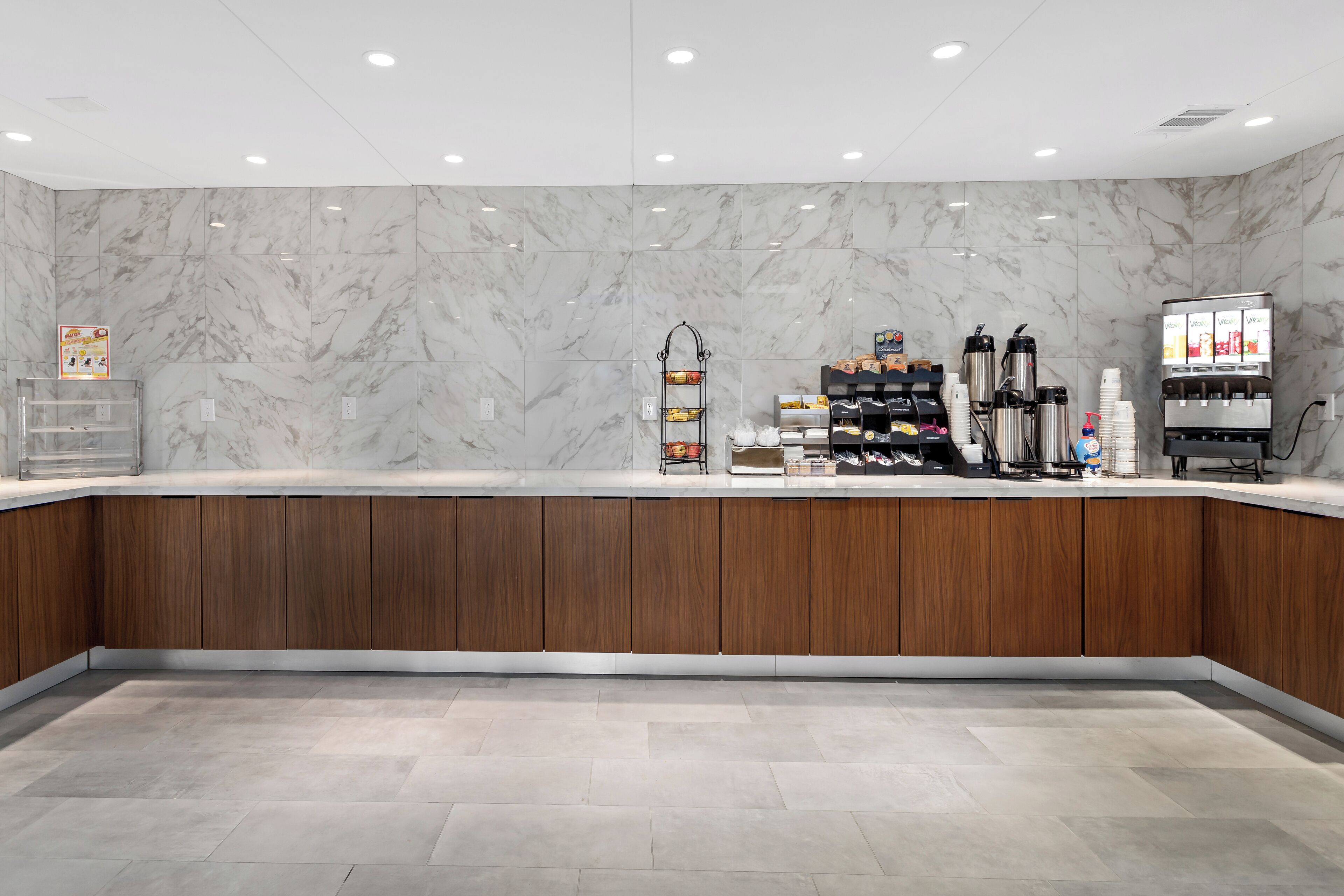 A modern reception area with marble walls, wooden counter, and various amenities like coffee machines and snack dispensers.