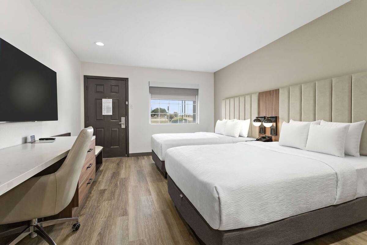 A hotel room with a desk, two beds, a TV, and a window with a view.