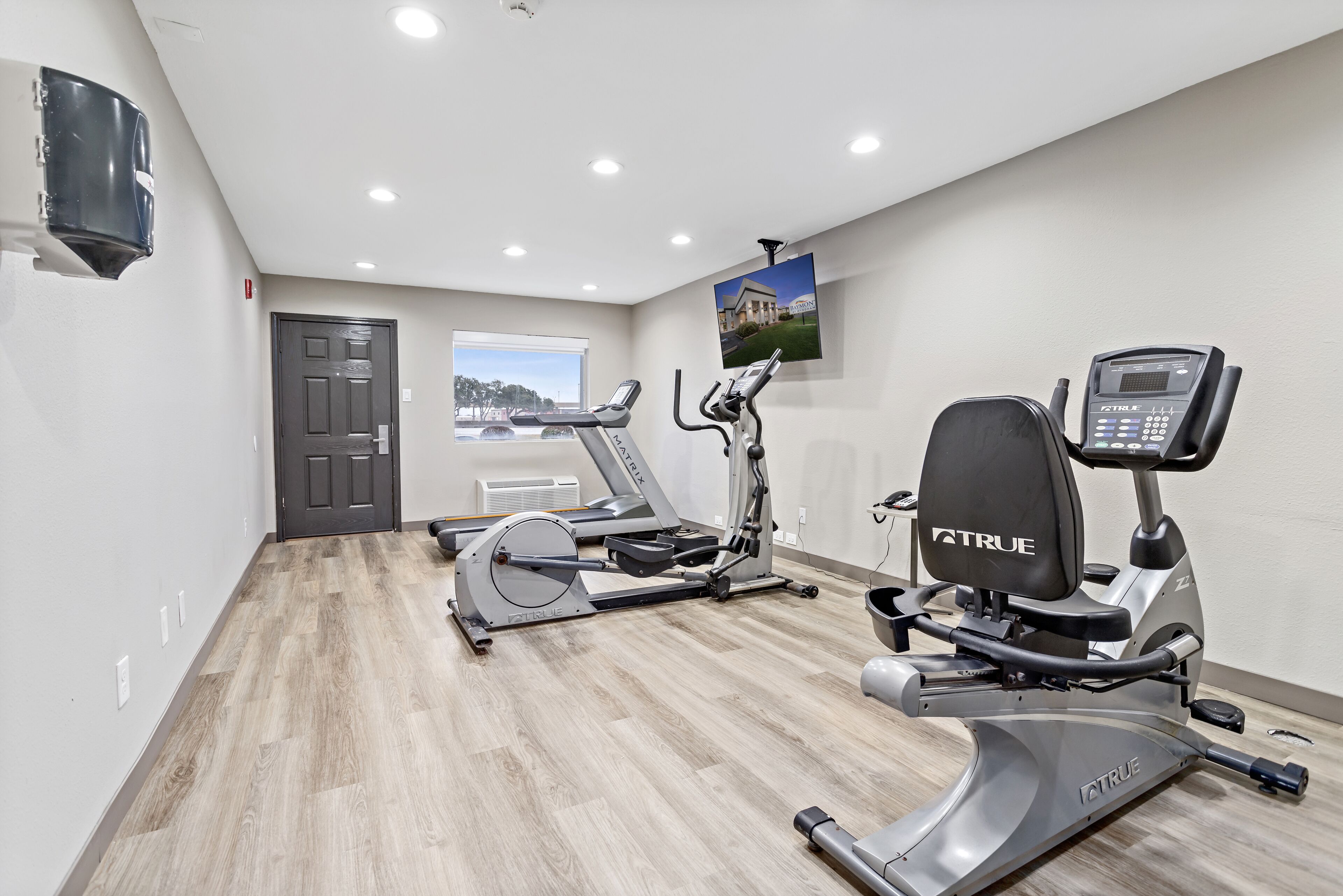 A gym with two treadmills, an elliptical, and a stationary bike, all with control panels.