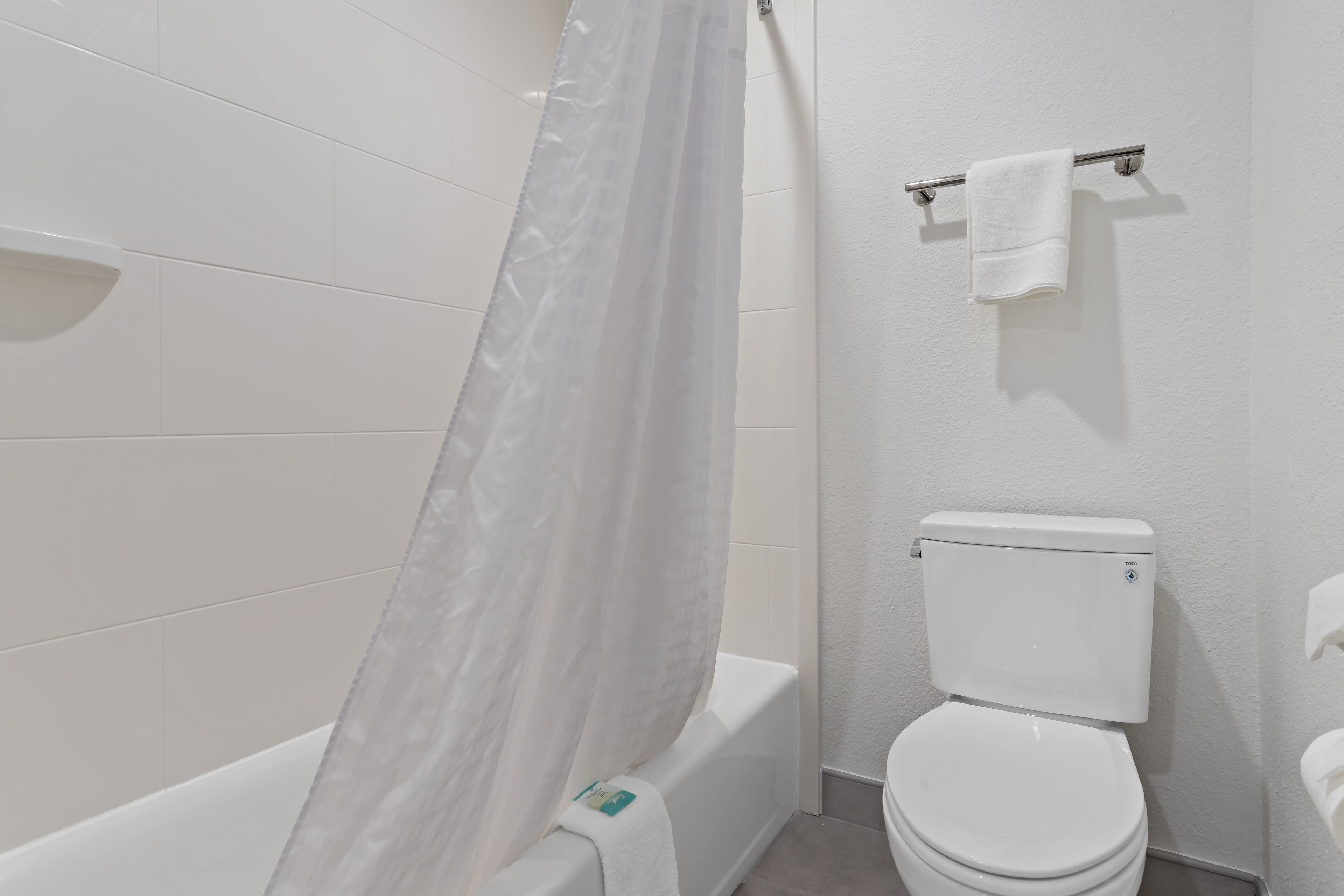Un baño con azulejos blancos, una bañera, un inodoro y un cortinero de ducha.