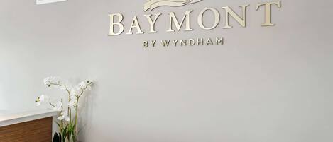 Un mostrador de recepción con un cartel que dice "Baymont by Wyndham" y un jarrón con orquídeas blancas.