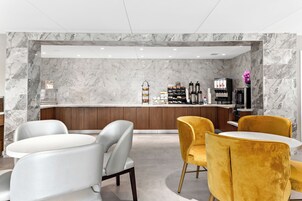 Uma área de bar moderna com paredes de mármore, balcão de madeira e espaço de estar com cadeiras brancas e amarelas.